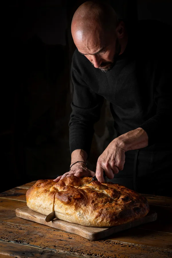 Braulio Simancas cortando un pan recién horneado sobre una tabla de madera