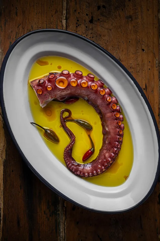 Una pata de pulpo en aceite de oliva, en una fuente esmaltada sobre madera antigua